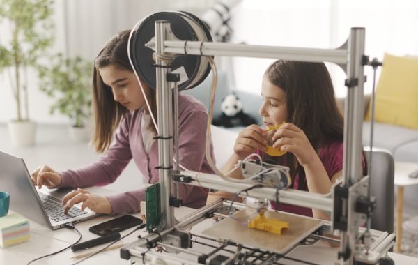 Young smart girls learning 3D printing at home, they are using a 3D printer and a laptop, science and education concept